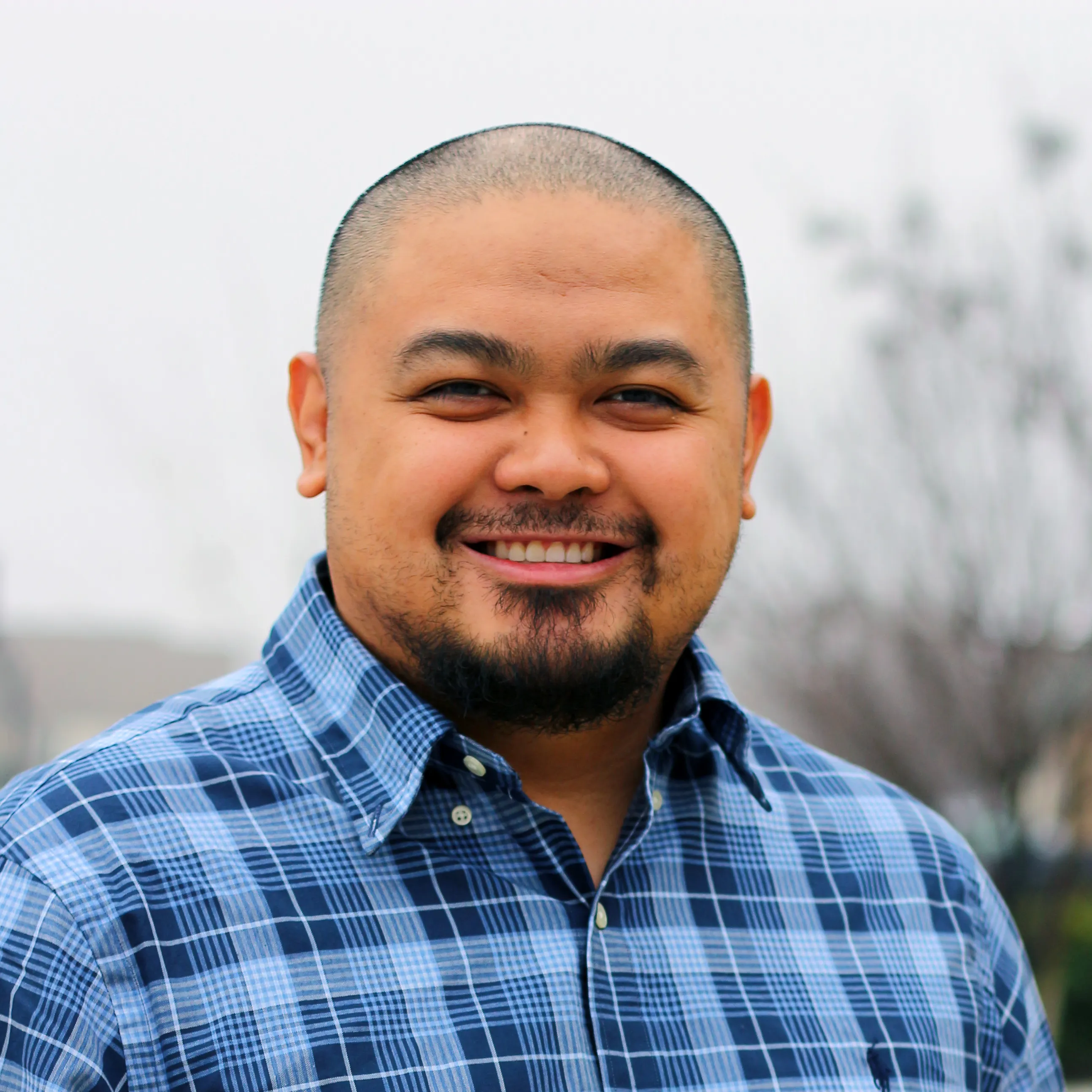 Jonathan Cruz smiling outdoors in a blue plaid button-down shirt.